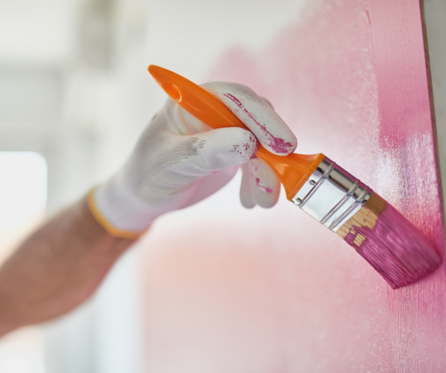 Hand, die eine Zimmerwand in Rosa streicht